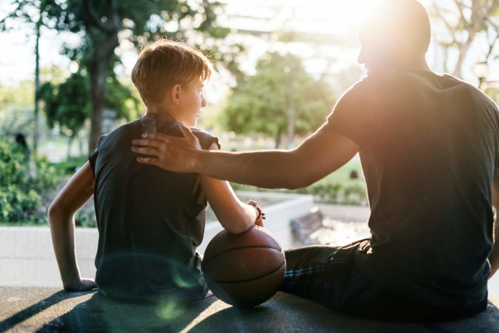 Un hombre da una palmada a su hijo tras un entrenamiento de baloncesto como metafora de la delegación